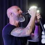 Chris Daughtry singing into a microphone during a live performance with dramatic lighting.
